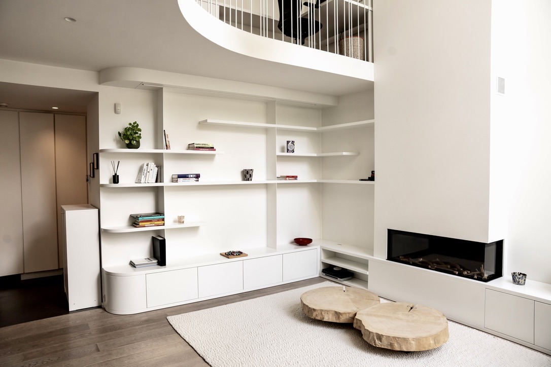 White lacquered library beneath a mezzanine, curved low unit and built-in fireplace