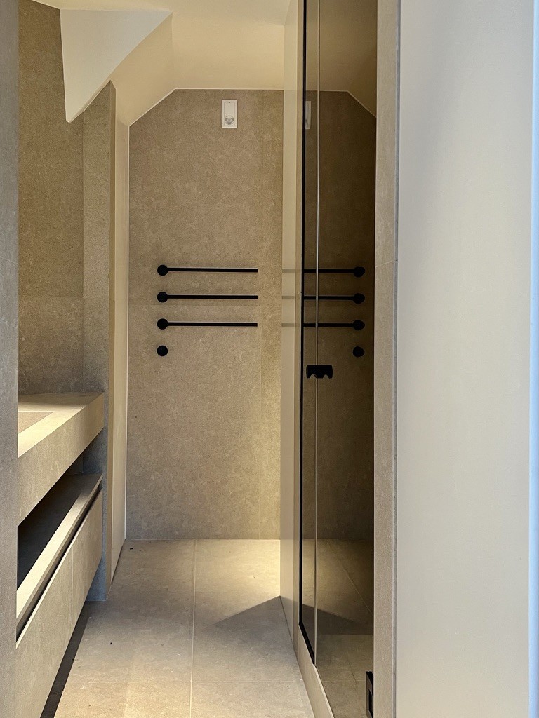 Walk-in shower in beige stone with black towel rails